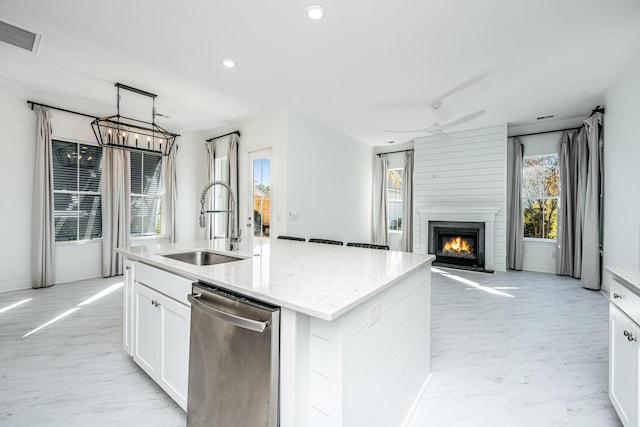 kitchen featuring sink, stainless steel dishwasher, an island with sink, a large fireplace, and white cabinetry