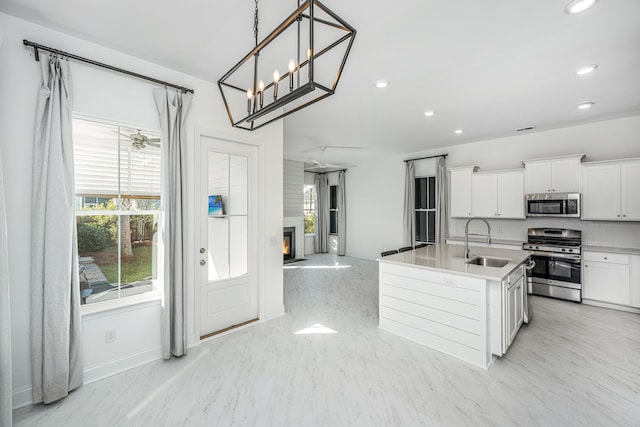 kitchen featuring appliances with stainless steel finishes, a kitchen island with sink, sink, white cabinetry, and hanging light fixtures