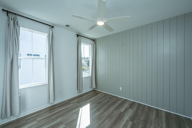 spare room featuring dark hardwood / wood-style flooring, ceiling fan, and wooden walls