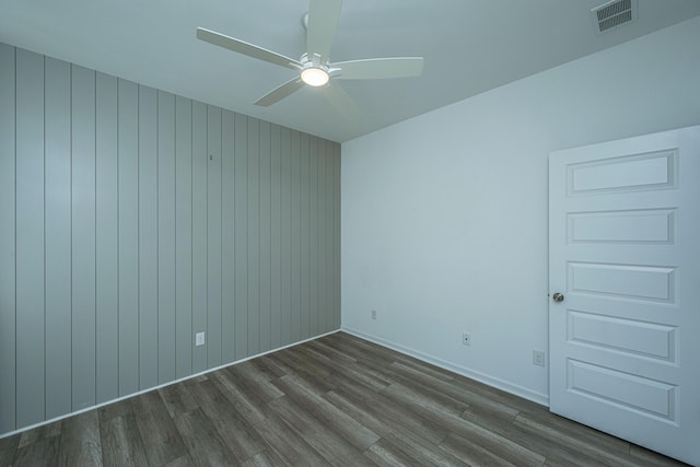 unfurnished room with ceiling fan, wood-type flooring, and wooden walls