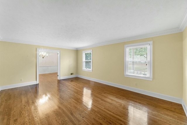 empty room with ornamental molding, plenty of natural light, wood-type flooring, and a notable chandelier