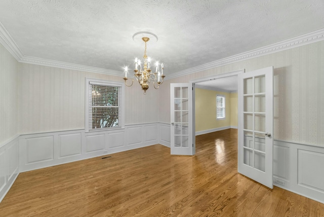 unfurnished dining area with hardwood / wood-style floors, french doors, a healthy amount of sunlight, and an inviting chandelier