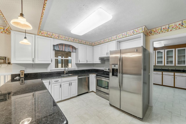 kitchen with dark stone counters, white cabinets, sink, hanging light fixtures, and appliances with stainless steel finishes