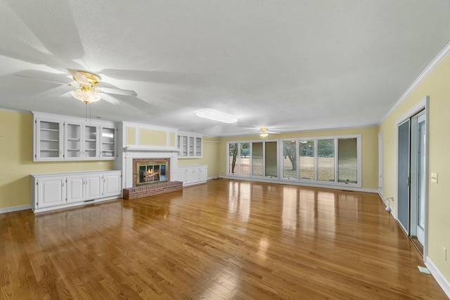 unfurnished living room featuring a textured ceiling, light hardwood / wood-style floors, a brick fireplace, and crown molding