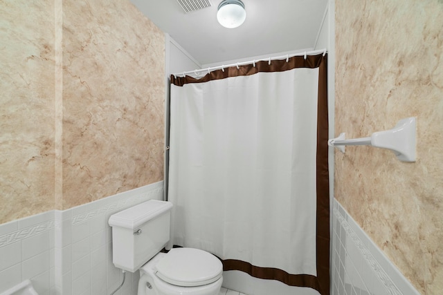 bathroom with toilet and tile walls