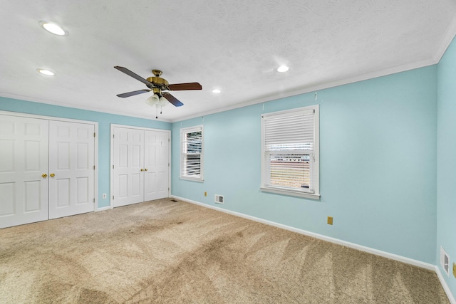 unfurnished bedroom with carpet, crown molding, ceiling fan, a textured ceiling, and multiple closets