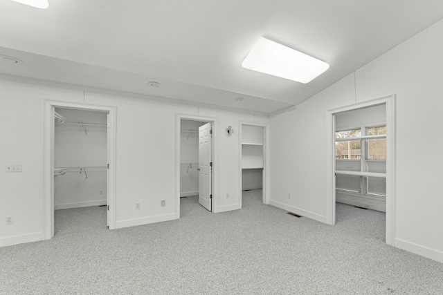 unfurnished bedroom featuring light carpet, vaulted ceiling, and a spacious closet