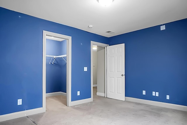 unfurnished bedroom with a closet, a spacious closet, visible vents, carpet floors, and baseboards