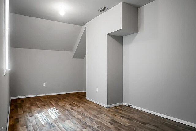 additional living space with wood finished floors, baseboards, vaulted ceiling, and visible vents