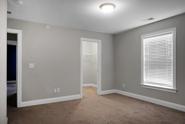 unfurnished bedroom with a closet, baseboards, visible vents, carpet floors, and a walk in closet