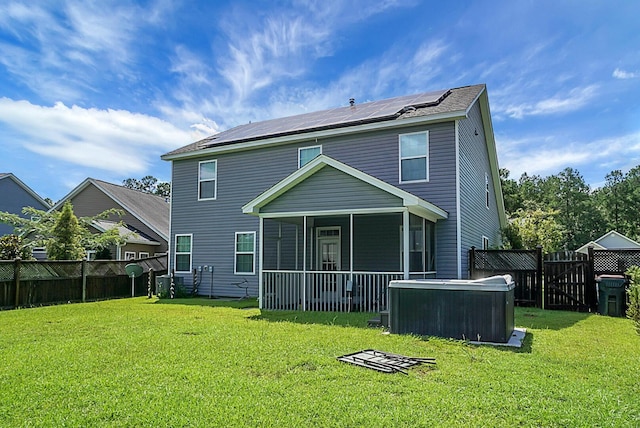 back of property with a sunroom, roof mounted solar panels, a fenced backyard, and a lawn