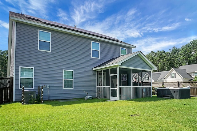 rear view of property featuring a hot tub, a sunroom, cooling unit, a lawn, and fence