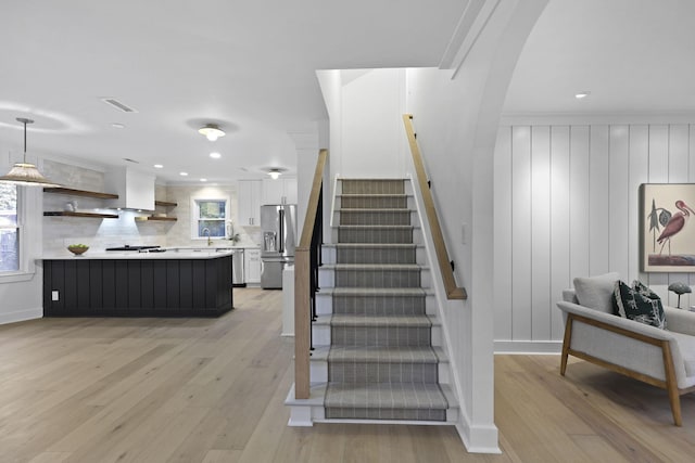 stairs with arched walkways, recessed lighting, wood finished floors, and visible vents