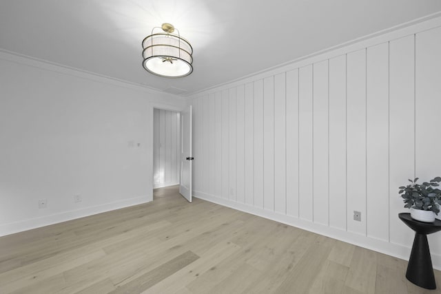 spare room featuring baseboards, ornamental molding, and light wood finished floors