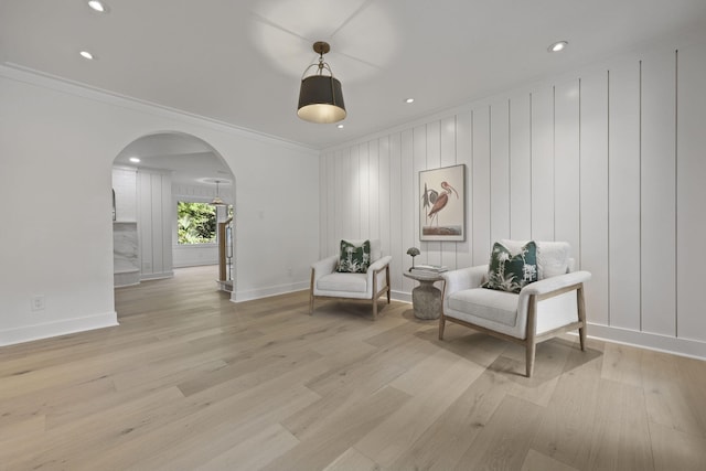 living area featuring crown molding, arched walkways, and light wood-style floors