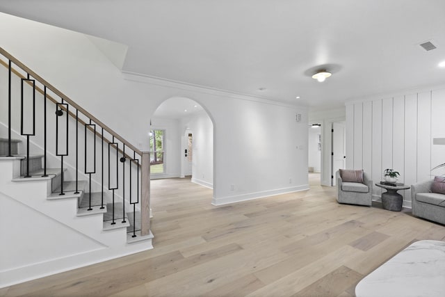 living room featuring crown molding, light wood-style floors, arched walkways, visible vents, and stairway