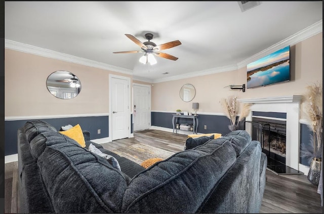 living room featuring a fireplace with raised hearth, wood finished floors, a ceiling fan, visible vents, and crown molding