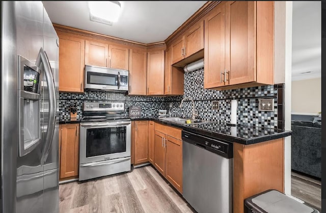 kitchen featuring dark countertops, light wood-style flooring, decorative backsplash, appliances with stainless steel finishes, and a sink