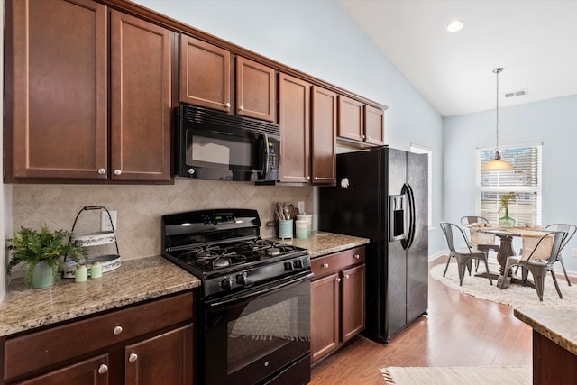 kitchen with light wood-type flooring, lofted ceiling, hanging light fixtures, black appliances, and tasteful backsplash