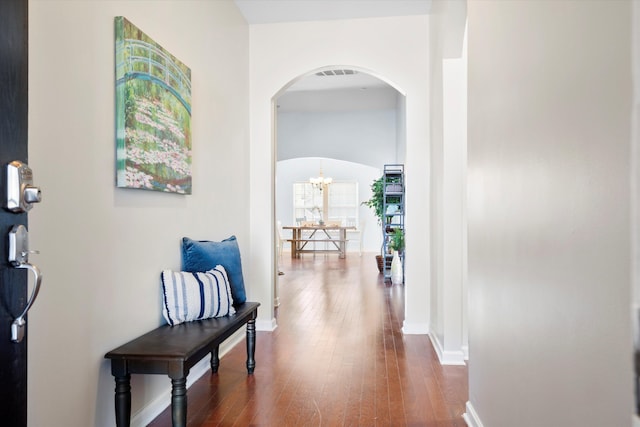 hall with visible vents, dark wood-type flooring, arched walkways, an inviting chandelier, and baseboards