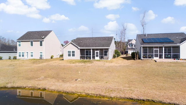 rear view of house featuring roof mounted solar panels, a lawn, and a sunroom