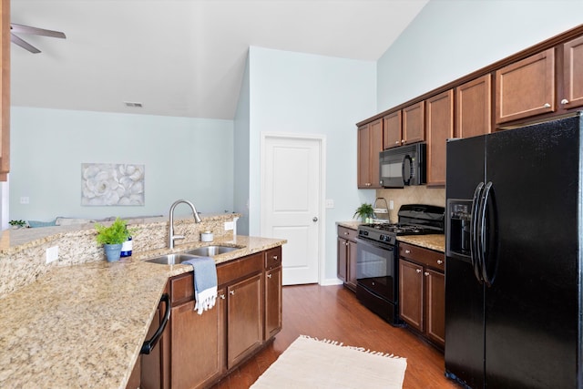 kitchen with visible vents, a sink, light stone counters, black appliances, and dark wood-style flooring