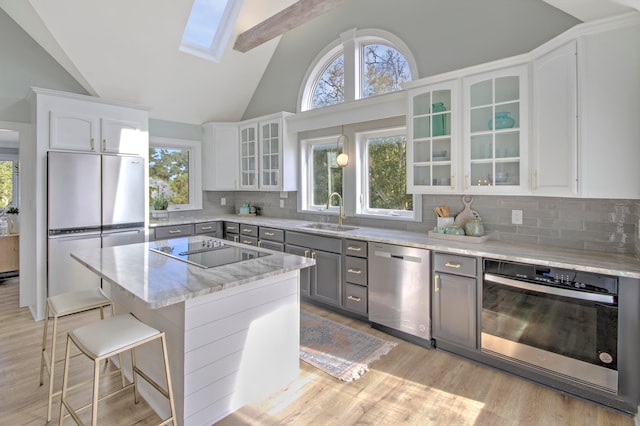 kitchen featuring tasteful backsplash, a skylight, white cabinetry, stainless steel appliances, and gray cabinetry