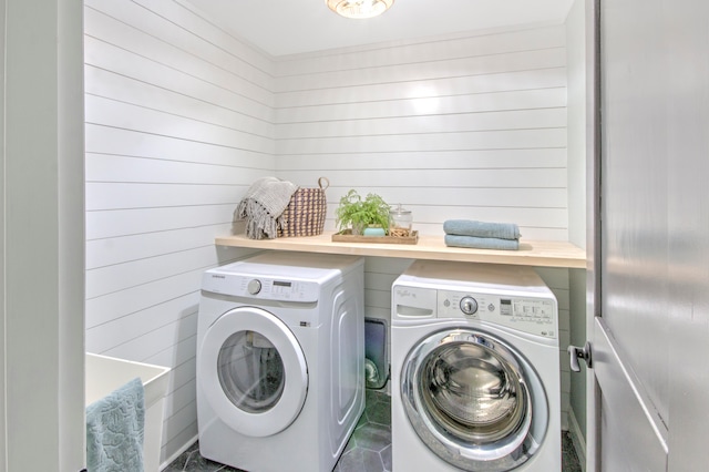 clothes washing area with wooden walls, dark tile floors, and washing machine and clothes dryer