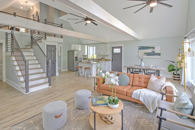 living room featuring light wood-type flooring, beamed ceiling, high vaulted ceiling, and ceiling fan with notable chandelier