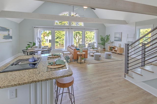 kitchen featuring a breakfast bar, beamed ceiling, light hardwood / wood-style flooring, light stone countertops, and ceiling fan