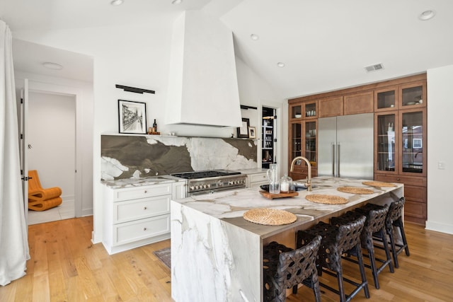 kitchen featuring high quality appliances, white cabinetry, a kitchen island with sink, and light stone counters