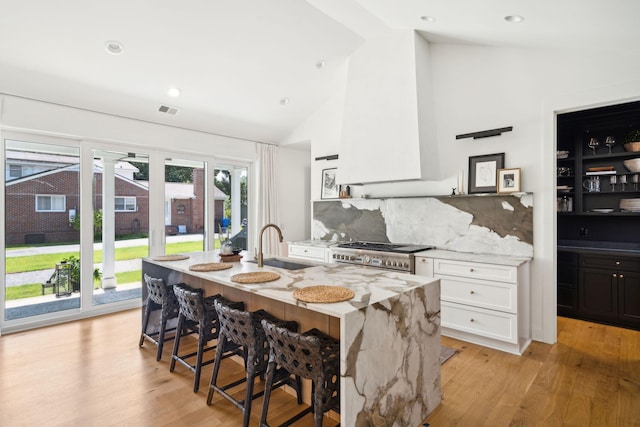 kitchen with sink, range, white cabinetry, light stone counters, and light wood-type flooring