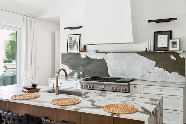 kitchen featuring lofted ceiling, sink, tasteful backsplash, light stone countertops, and white cabinets