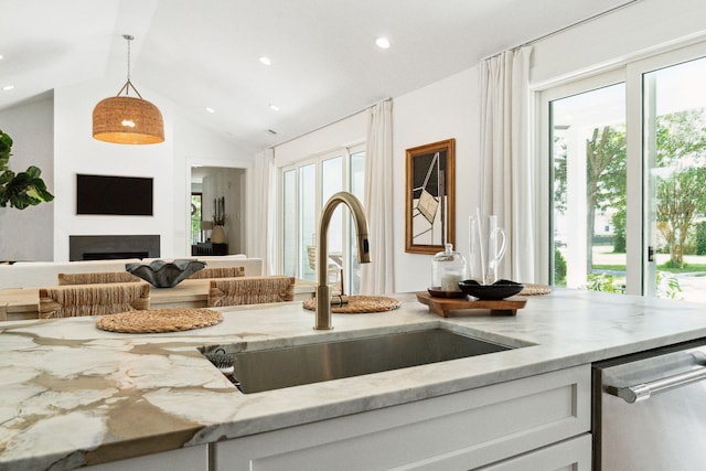 kitchen featuring pendant lighting, dishwasher, lofted ceiling, sink, and light stone counters