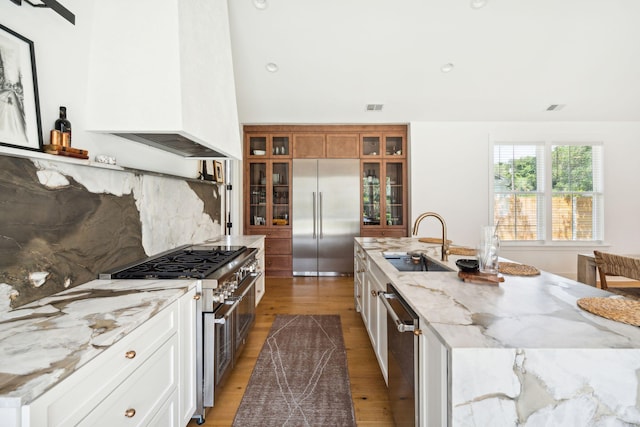 kitchen with sink, premium appliances, light stone countertops, a kitchen island with sink, and white cabinets