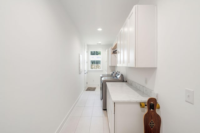 clothes washing area featuring light tile patterned floors, washer and clothes dryer, and cabinets