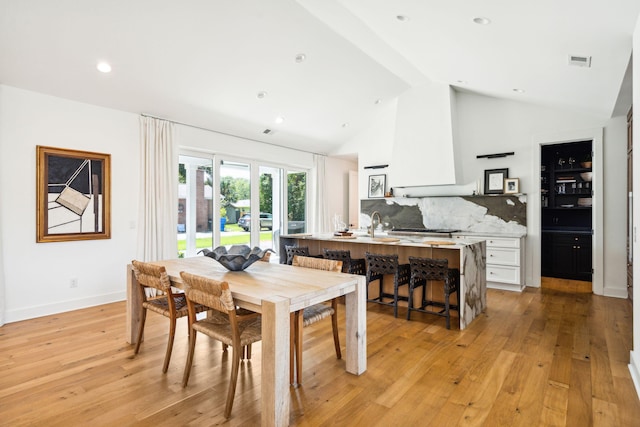 dining area with high vaulted ceiling, sink, and light hardwood / wood-style floors