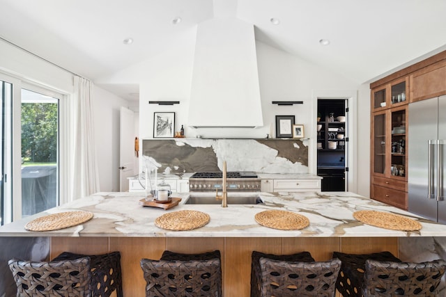 kitchen with premium range hood, lofted ceiling, stainless steel built in fridge, and a breakfast bar area