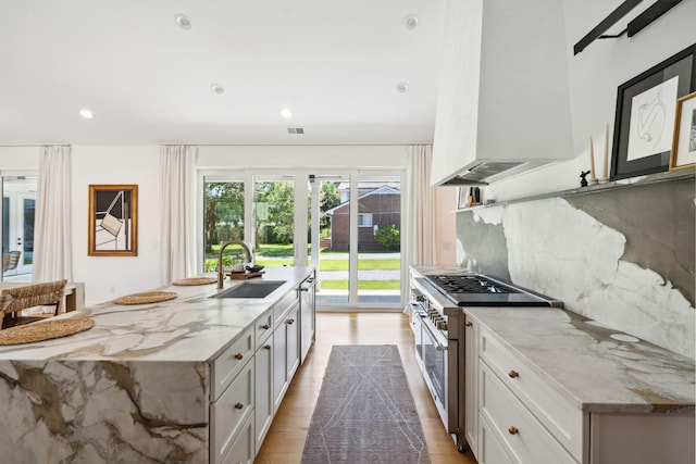 kitchen with wall chimney exhaust hood, sink, white cabinetry, appliances with stainless steel finishes, and light stone countertops