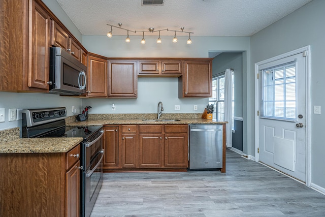 kitchen with sink, stainless steel appliances, a textured ceiling, and light stone countertops