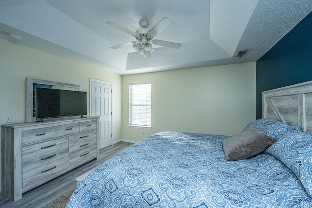 bedroom with ceiling fan, a tray ceiling, a textured ceiling, and light wood-type flooring