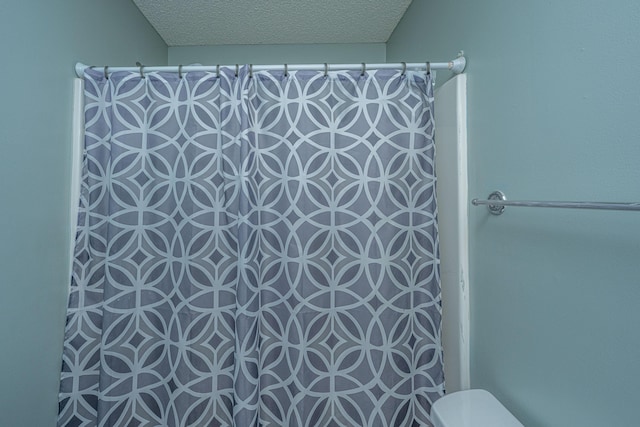 bathroom with toilet, a textured ceiling, and a shower