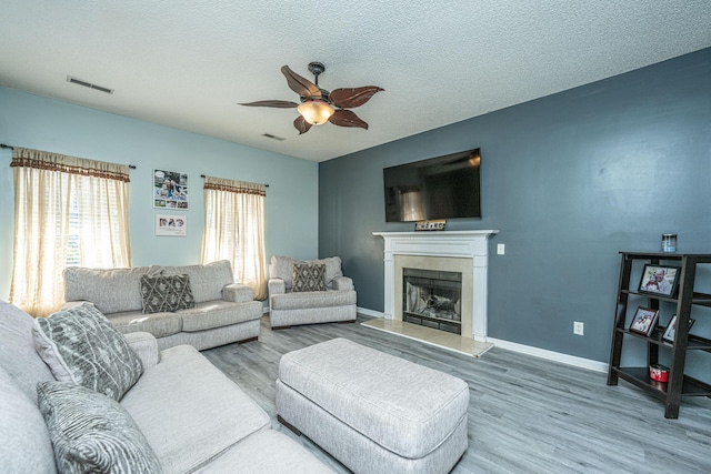 living room featuring ceiling fan, wood-type flooring, a premium fireplace, and a textured ceiling