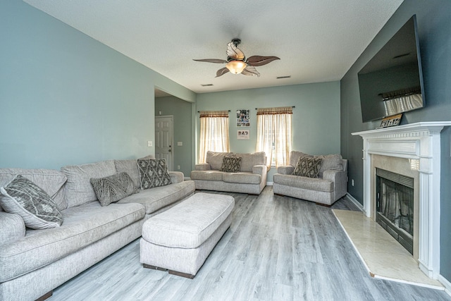 living room featuring a textured ceiling, wood-type flooring, a premium fireplace, and ceiling fan