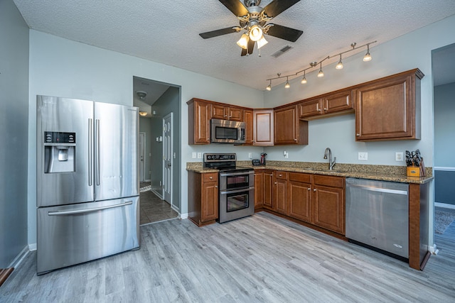 kitchen featuring appliances with stainless steel finishes, sink, light hardwood / wood-style floors, light stone countertops, and a textured ceiling