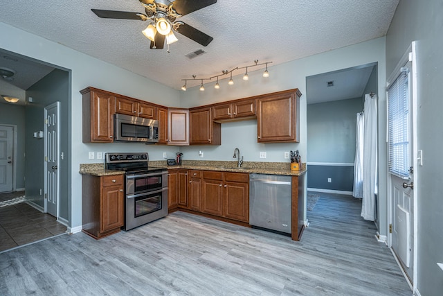 kitchen featuring appliances with stainless steel finishes, sink, light hardwood / wood-style floors, light stone countertops, and a textured ceiling