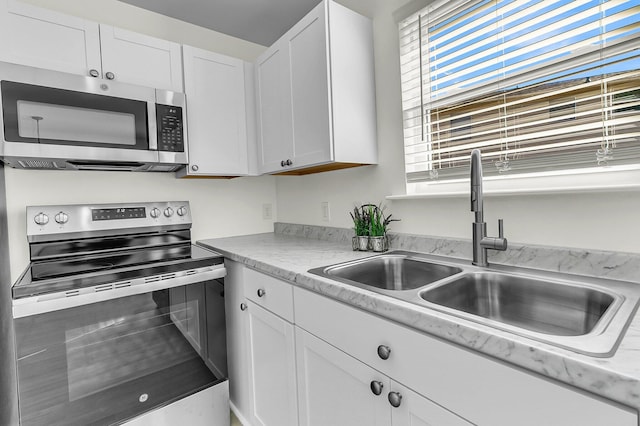 kitchen featuring appliances with stainless steel finishes, white cabinetry, light countertops, and a sink