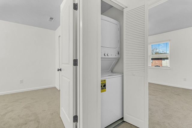 clothes washing area featuring laundry area, stacked washer and dryer, baseboards, and light carpet