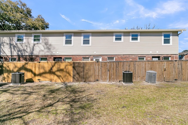 rear view of house with a yard, brick siding, central AC, and fence