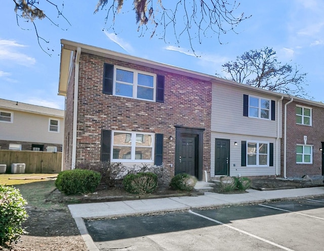 townhome / multi-family property with brick siding, uncovered parking, and fence